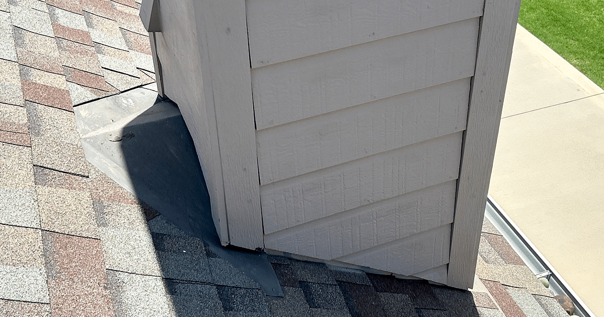 The image shows a close-up view of a residential roof featuring metal flashing around a brick chimney and plumbing vent pipe. This properly installed flashing plays a critical role in preventing roof leaks by directing water away from vulnerable areas and ensuring a watertight seal around roof penetrations.
