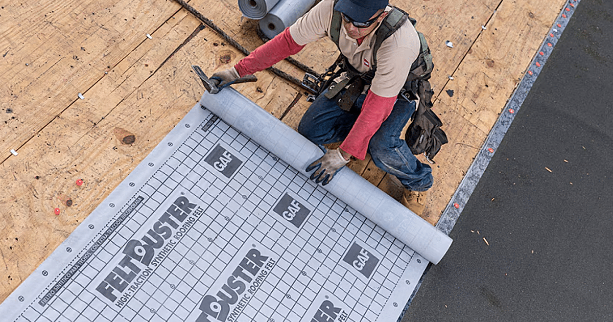 A roofing contractor is skillfully installing synthetic underlayment on a roof deck, ensuring proper overlap technique for optimal water resistance and protection against weather exposure. This installation is a crucial part of the roofing system, providing a waterproof seal beneath the asphalt shingles to prevent moisture damage and enhance the structural integrity of the entire roof.