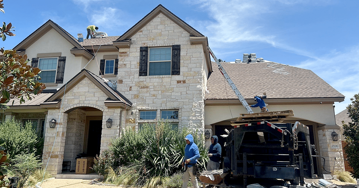 The image depicts roofing contractors using specialized equipment to safely access a steep, multi-story roof for a roof replacement project. The professionals are engaged in the roof replacement process, which can involve various factors that drive up roof replacement costs, such as labor expenses and the complexity of the roofing system.